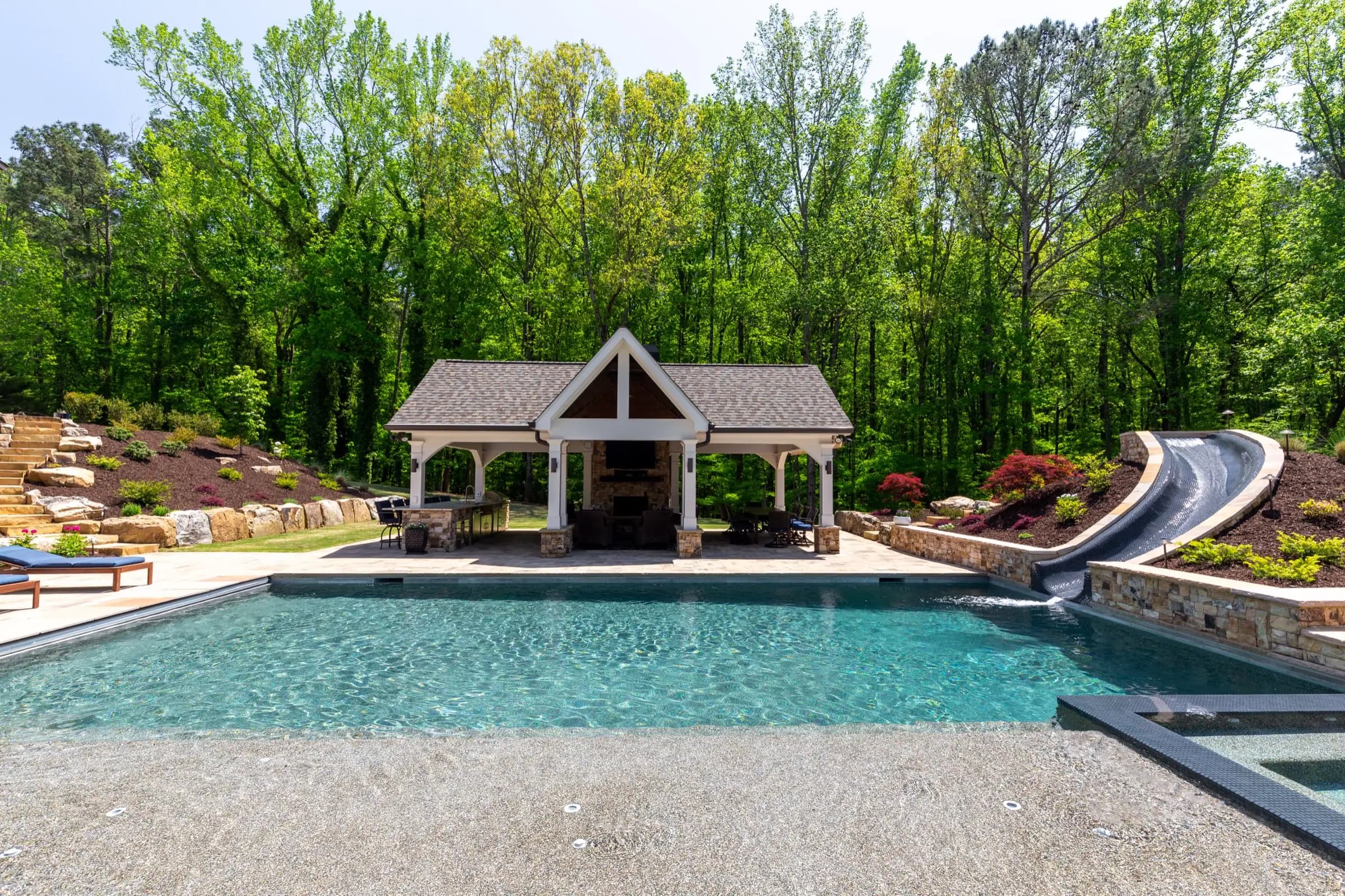 The Batchelor pool and pavilion in Roswell, with the covered outdoor kitchen, fireplace, and water slide built into stone at one edge