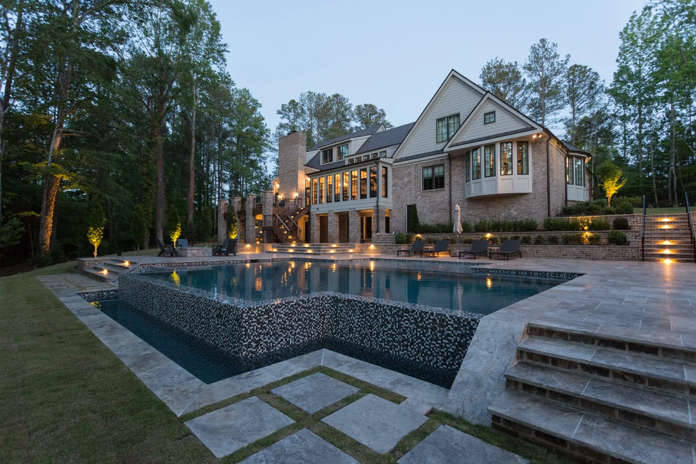 Raised vanishing-edge pool with wide travertine steps at dusk at the Chadwell project in Roswell