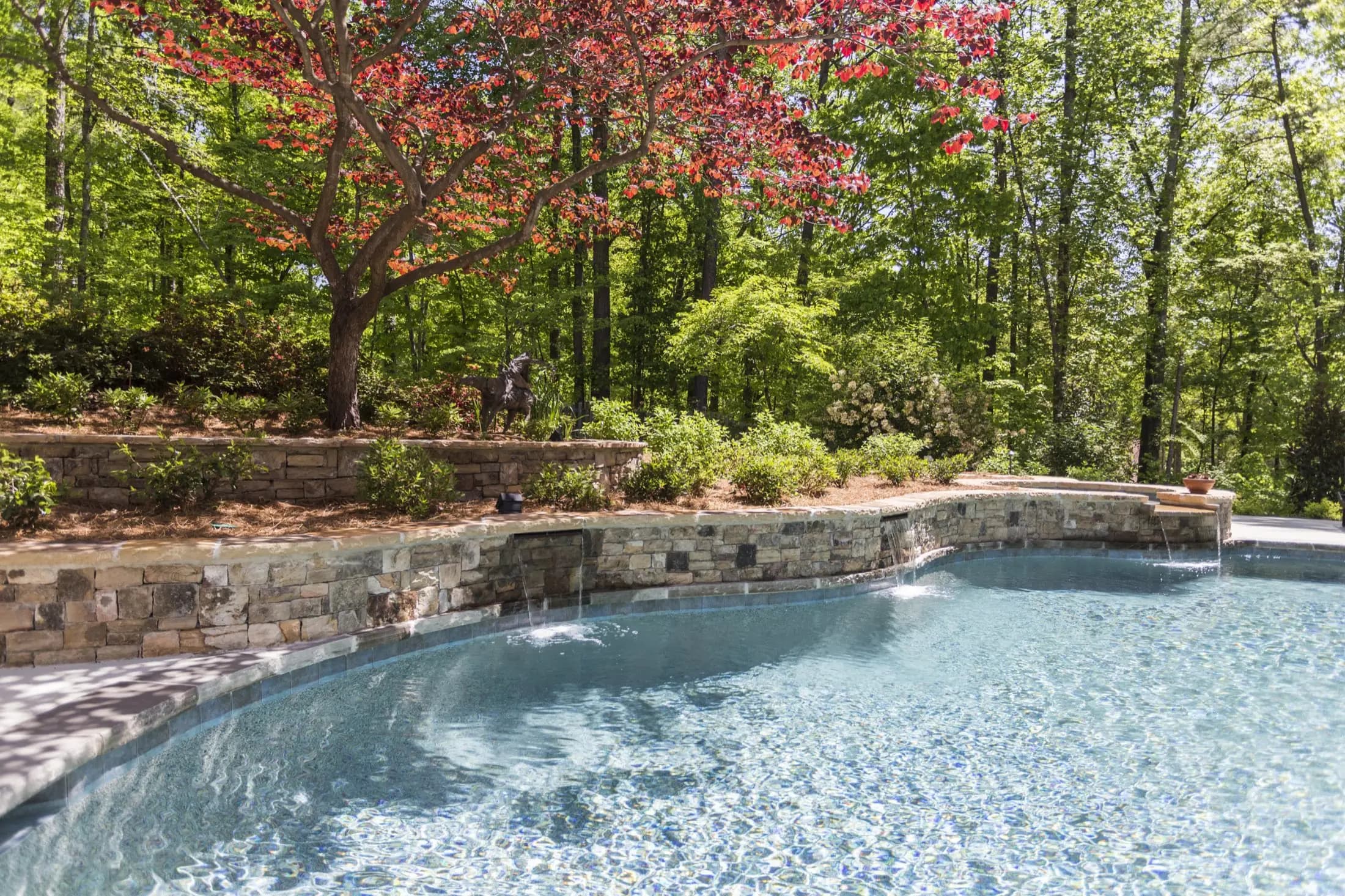 Stacked-stone waterfall wall under a red Japanese maple at the Starke project in Johns Creek