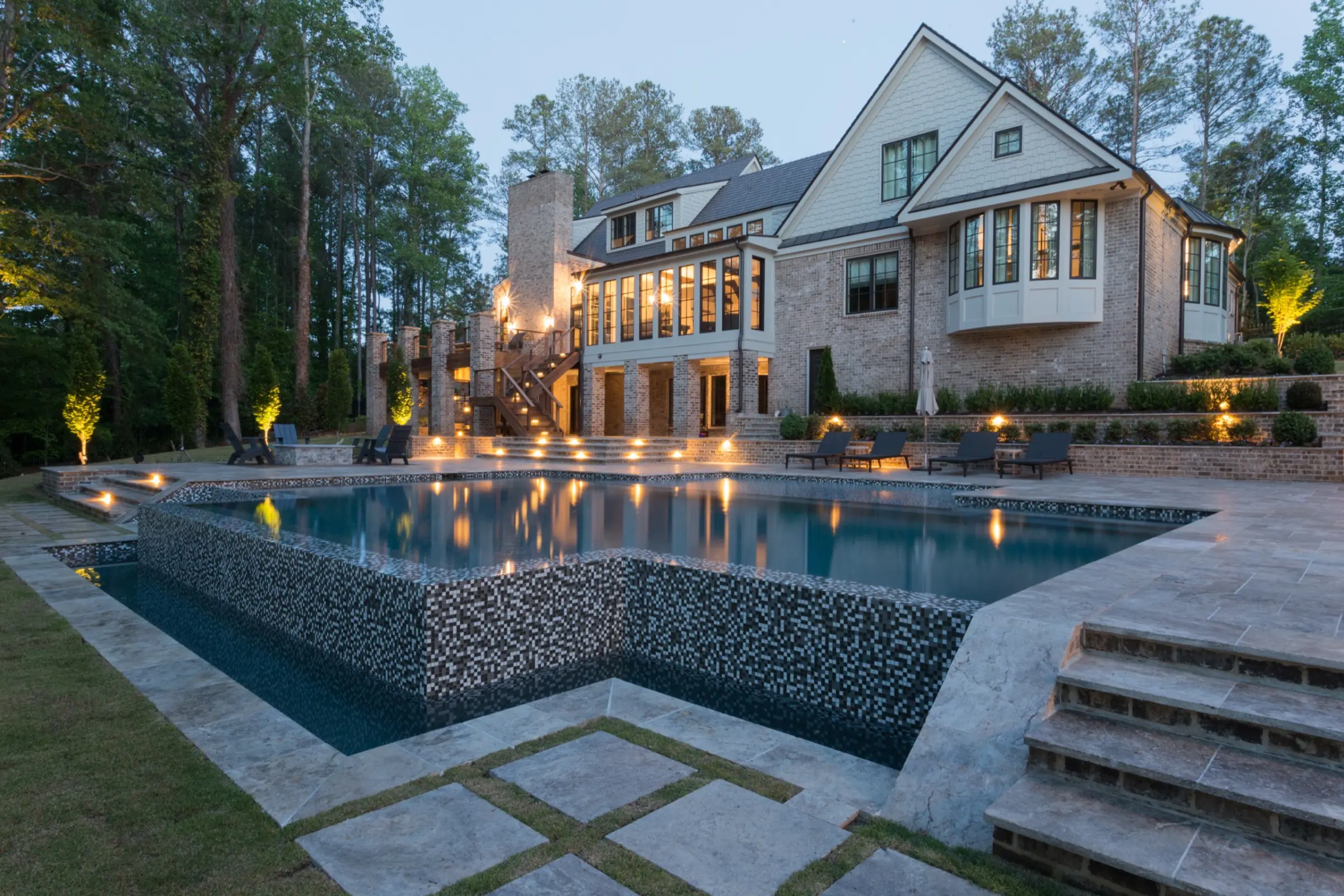 A custom pool with glass-tile spillway at twilight below a brick estate in Roswell, built by Atlantis Pools